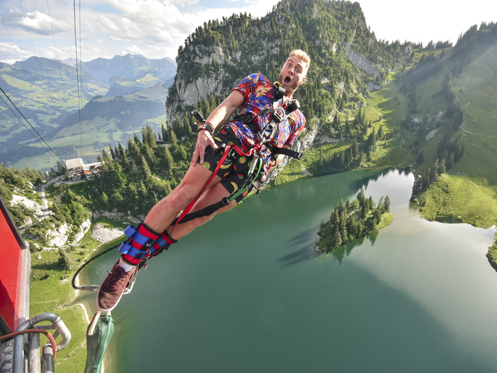 A man wearing a colorful mismatched outfit springs sideways from the gondola during the Stockhorn Bungy Jump