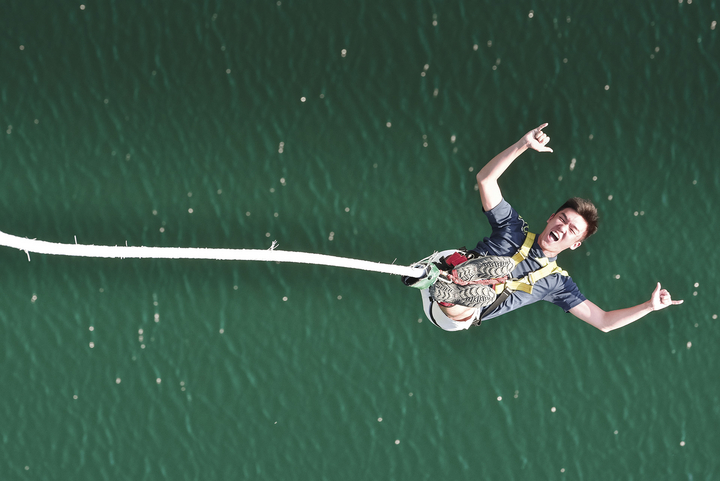 A smiling man displays the "hang loose" sign on each hand as he rebounds during the Stockhorn Bungy Jump