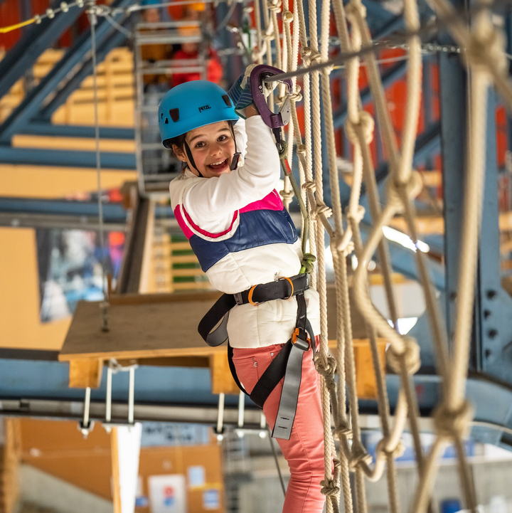 A young girl stands on a rope ladder and grabs the safety cable as she navigates a course at the Indoor Ropes Park in Grindelwald